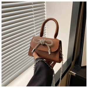 Détail du sac en cuir marron avec nœud en strass et bandoulière chaîne argent