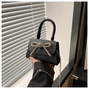 Détail du mini sac noir en cuir grainé avec un nœud en strass étincelant sur le devant