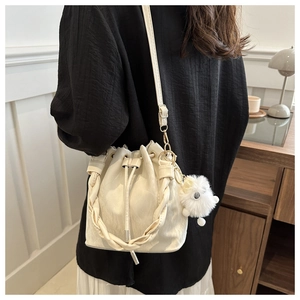 Détail du sac seau crème avec poignée tressée et breloque en peluche décorative