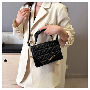Détail du sac matelassé noir avec fermoir doré et poignée plissée sur une veste chic