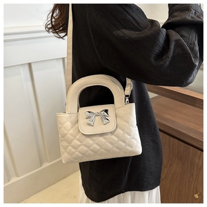 Detail view of cream quilted crossbody bag with a metallic silver bow on the flap