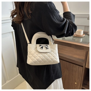 Detail of quilted crossbody bag with bow hardware and round handle in beige finish