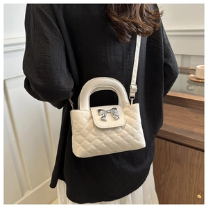 Detail of white quilted handbag with a silver bow ornament and crossbody strap