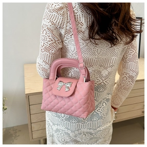 Detailed view of pink quilted handbag with silver bow charm worn as a crossbody bag