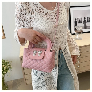 Pink quilted crossbody bag with silver bow detail shown on a model in a home setting