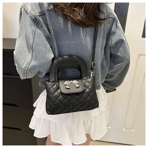 Close-up of quilted black crossbody bag with silver bow detail worn by a model