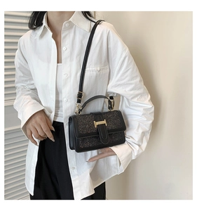 Detail of black glitter crossbody bag with gold H clasp worn by model in white shirt