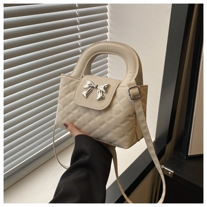 Detailed view of cream bow-decorated crossbody bag with elegant diamond quilted pattern