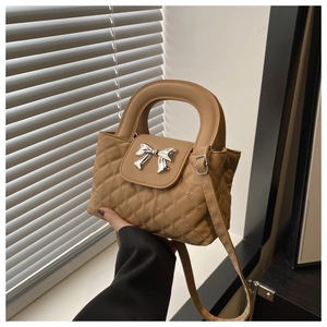 Close-up of khaki quilted handbag featuring a silver bow metal clasp and top handle