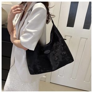 Detail of a black textured hobo tote bag worn on shoulder by a model in a minimalist room