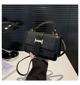 Close-up of black handbag featuring shiny sequins and golden H-shaped buckle detail