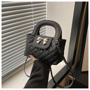 Close-up of black quilted leather handbag featuring a golden bow metal clasp and handle