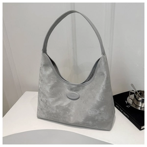 Close-up of grey textured hobo bag featuring an oval brand logo plate on a desk