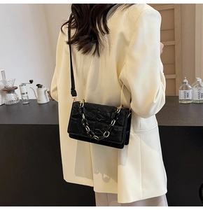 Detail of black pleated texture shoulder bag with gold chain and crossbody strap worn by model