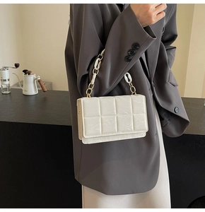 Detail of white quilted rectangular handbag with gold metal and resin chain strap worn by model