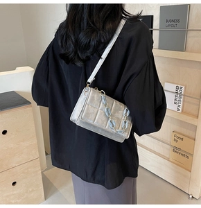 Silver quilted crossbody bag with light blue chain strap shown on model in a cozy room
