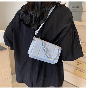Detail of light blue quilted square crossbody bag with decorative chain and strap