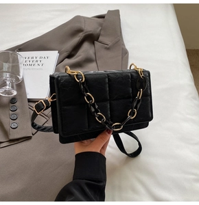 Détail du sac carré en cuir matelassé noir avec chaîne dorée et texture élégante