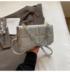 Détail d'un sac à main matelassé en velours gris avec des chaînes bleu et or