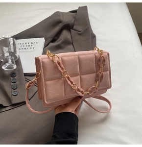Detail of pink quilted handbag featuring dual metallic and matte chain straps on a white desk
