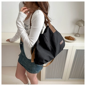Large black canvas tote bag with brown straps worn by a model in a cozy home setting