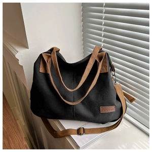 Detail of black canvas tote bag with brown straps and leather fashion label on window sill