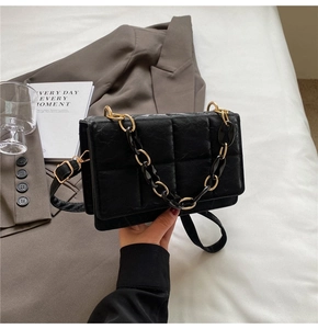 Detail of black quilted chain bag with gold accents shown in a modern lifestyle setting