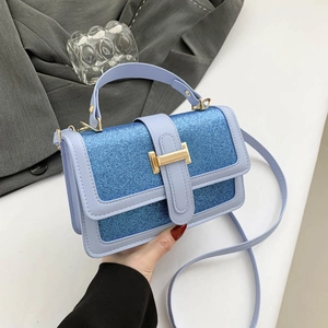 Blue leather small square handbag with glitter panel and golden clasp, held by a model
