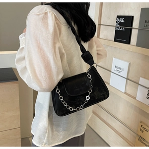 Détail d'un sac sous le bras en cuir noir avec chaîne florale argentée sur étagère