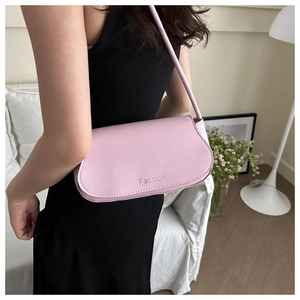 Side view of a minimalist pale pink shoulder bag worn by a model in a modern room