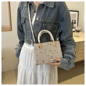 Close-up of woven straw handbag with floral embroidery and white round handle