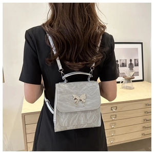 Silver metallic bucket bag with bow buckle worn by a model in a minimalist black dress