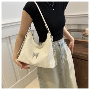 Détail du sac fourre-tout blanc avec papillon et bandoulière chaîne portée à l'épaule