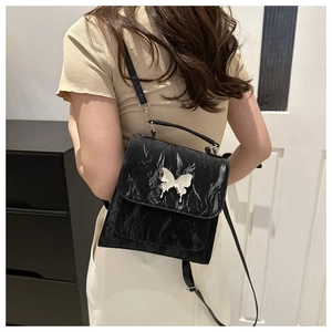 Detail of black pebbled backpack featuring a large silver butterfly metal buckle