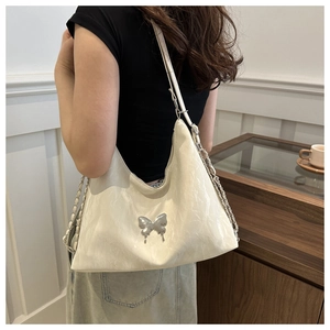 Détail d'un sac à bandoulière blanc en demi-lune avec un ornement papillon en métal argenté