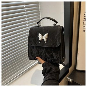 Close-up of black pleated leather handbag featuring a silver butterfly metal ornament