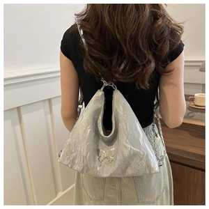Détail de la texture plissée argentée du sac à bandoulière avec papillon en métal et chaîne