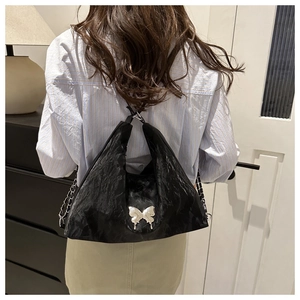 Détail du sac plissé noir avec pendentif papillon argenté et bandoulière en chaîne métal