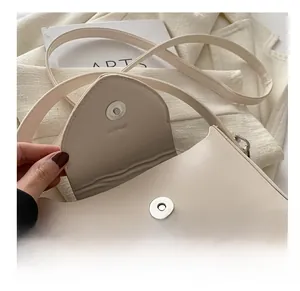 Detailed close-up of the magnetic metal clasp and smooth leather texture of the off-white bag