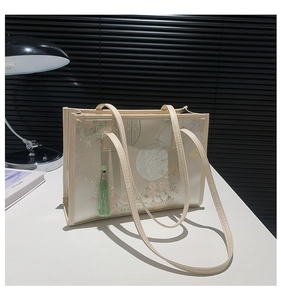 Detailed view of cream tote bag featuring traditional Chinese floral prints and a green tassel