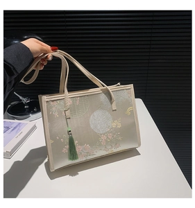 Detailed embroidery of plum blossoms on a beige tote bag with a green tassel charm