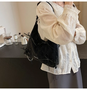 Détail du sac à épaule en satin noir avec nœuds décoratifs et chaîne argentée