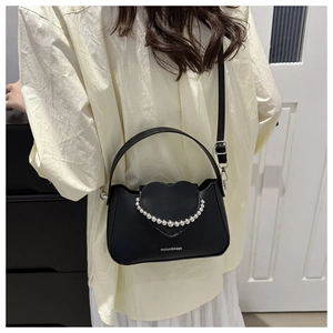 Detail view of the black heart-shaped handbag with white faux pearl chain decoration
