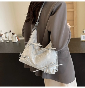 Détail d'un sac à bandoulière argenté texturé avec nœuds et bandoulière en chaîne