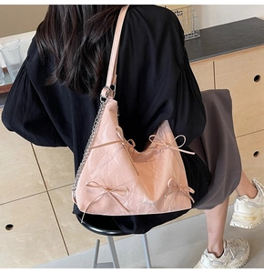 Détail de sac hobo rose avec nœuds, texte mode et accents de chaîne métallique sur la bandoulière
