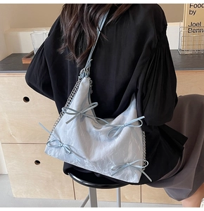 Détail du sac à main bleu clair avec nœuds, chaîne argentée et texture plissée