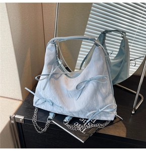 Gros plan d'un sac à bandoulière bleu clair plissé avec nœuds décoratifs et chaîne argent