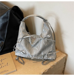 Détail du sac hobo argenté avec nœuds décoratifs et texture en cuir plissé métallique