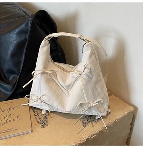 Détail du sac à main crème avec nœuds papillon, texture plissée et lettrage fashion