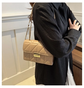 Détail d'un sac à bandoulière matelassé marron clair avec fermoir doré sur un mannequin